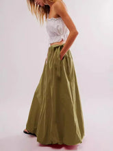 Load image into Gallery viewer, Woman wearing Boho maxi skirt with side bow tie and pockets in olive green. Side view hands in pockets.- Gypsy Collection women's skirt